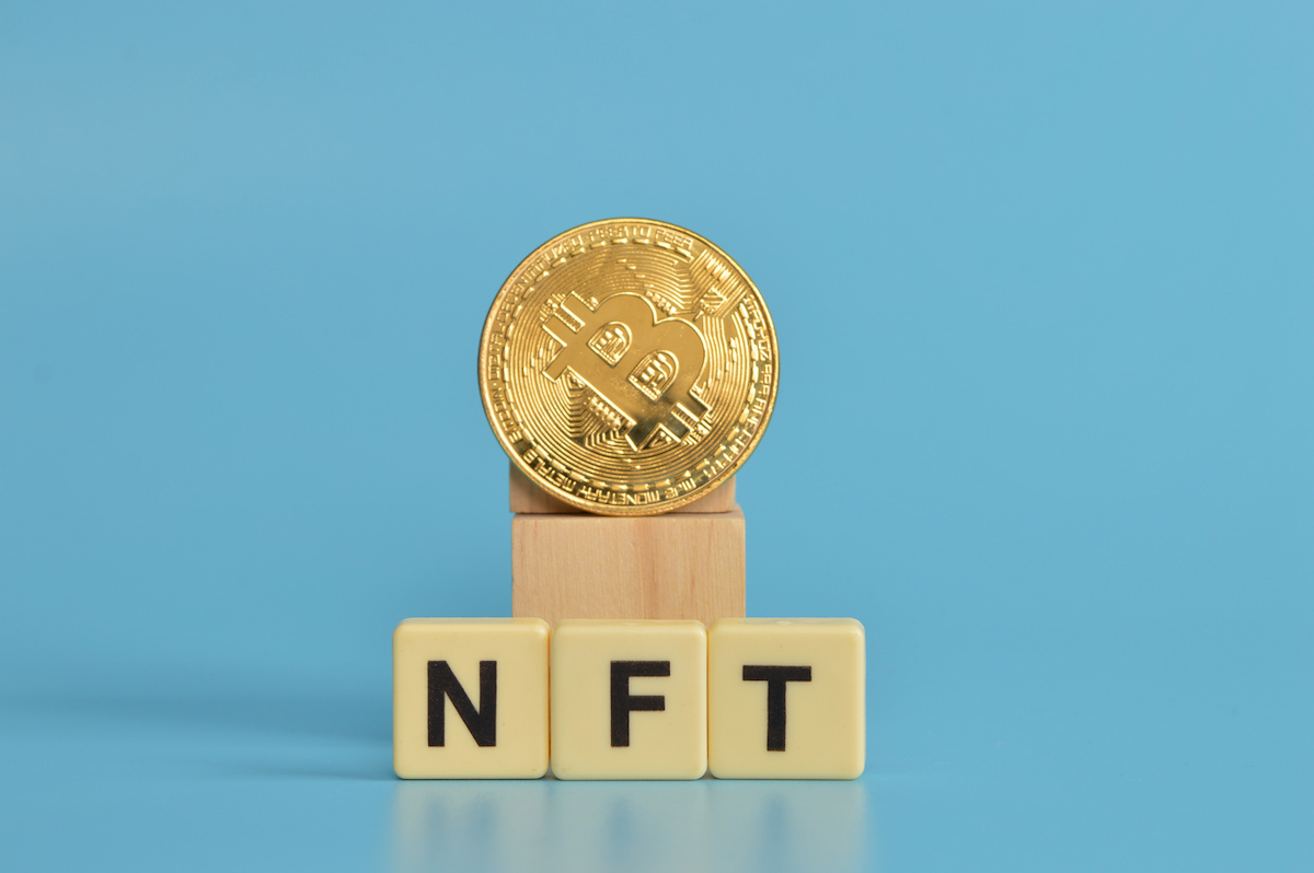 Bitcoin coin sitting on top of a wooden block with the word "NFT" written on it